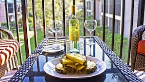 A table with a bottle of wine, two glasses, and a plate of food on a balcony. - White Sands & Seashells, 1 BR 2nd Fl (Siesta Key)