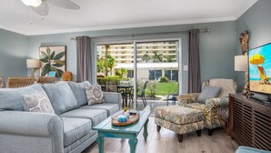 A living room with a grey sofa, a patterned armchair, a wooden coffee table, and a television. - Jamaica Royale Townhome #2 - Steps From Beach (Siesta Key)