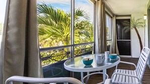 A balcony with a glass table, two white chairs, and a view of palm trees. - Jamaica Royale Townhome #2 - Steps From Beach (Siesta Key)