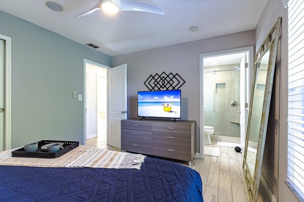 Une chambre à coucher avec un lit, une commode, un téléviseur et une salle de bain visible à travers une porte ouverte.