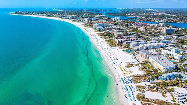 Eine Luftaufnahme einer Küstenstadt mit einem langen Sandstrand, zahlreichen Hotels und klarem, blauem Wasser.