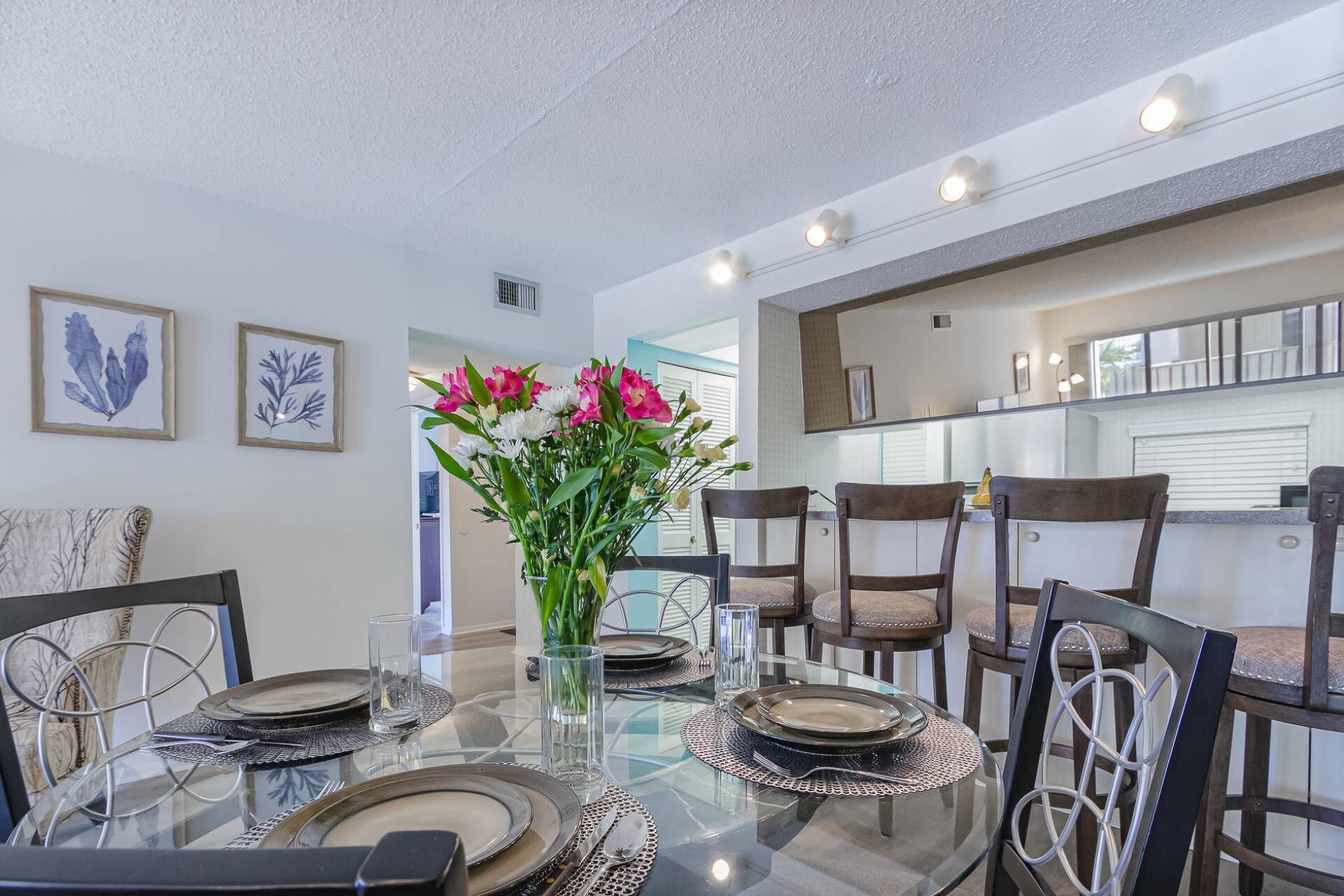 A dining area with a glass table set for four, surrounded by dark wooden chairs.