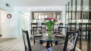 Un coin repas avec une table ronde en verre, six chaises et un vase de fleurs.