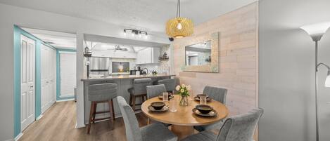 A modern kitchen with a central island, grey upholstered chairs around a wooden dining table, and a hanging light fixture.