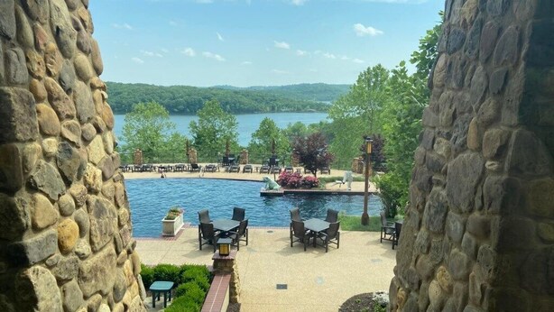 A stone-walled patio overlooking a lake with outdoor seating and a swimming area.