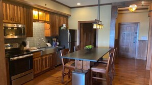 A kitchen with wooden cabinets, stainless steel appliances, a dining table with chairs, and a trash can.