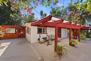 A covered outdoor area with a red pergola, a bench, and exercise equipment. - The Good Land Getaway (Moreno Valley)