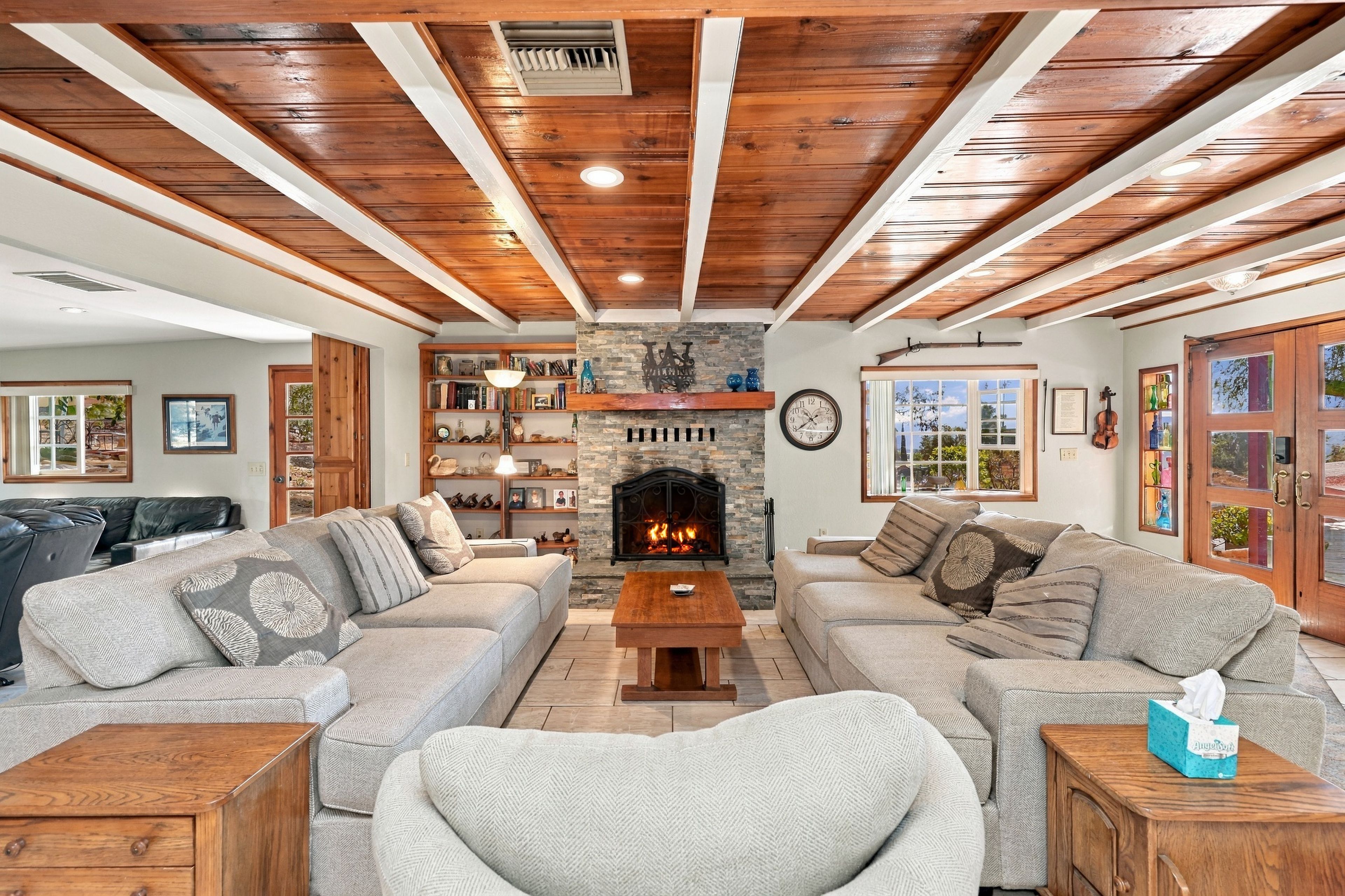 A cozy living room with a fireplace, wooden beams, and a fireplace mantel with decorative items.