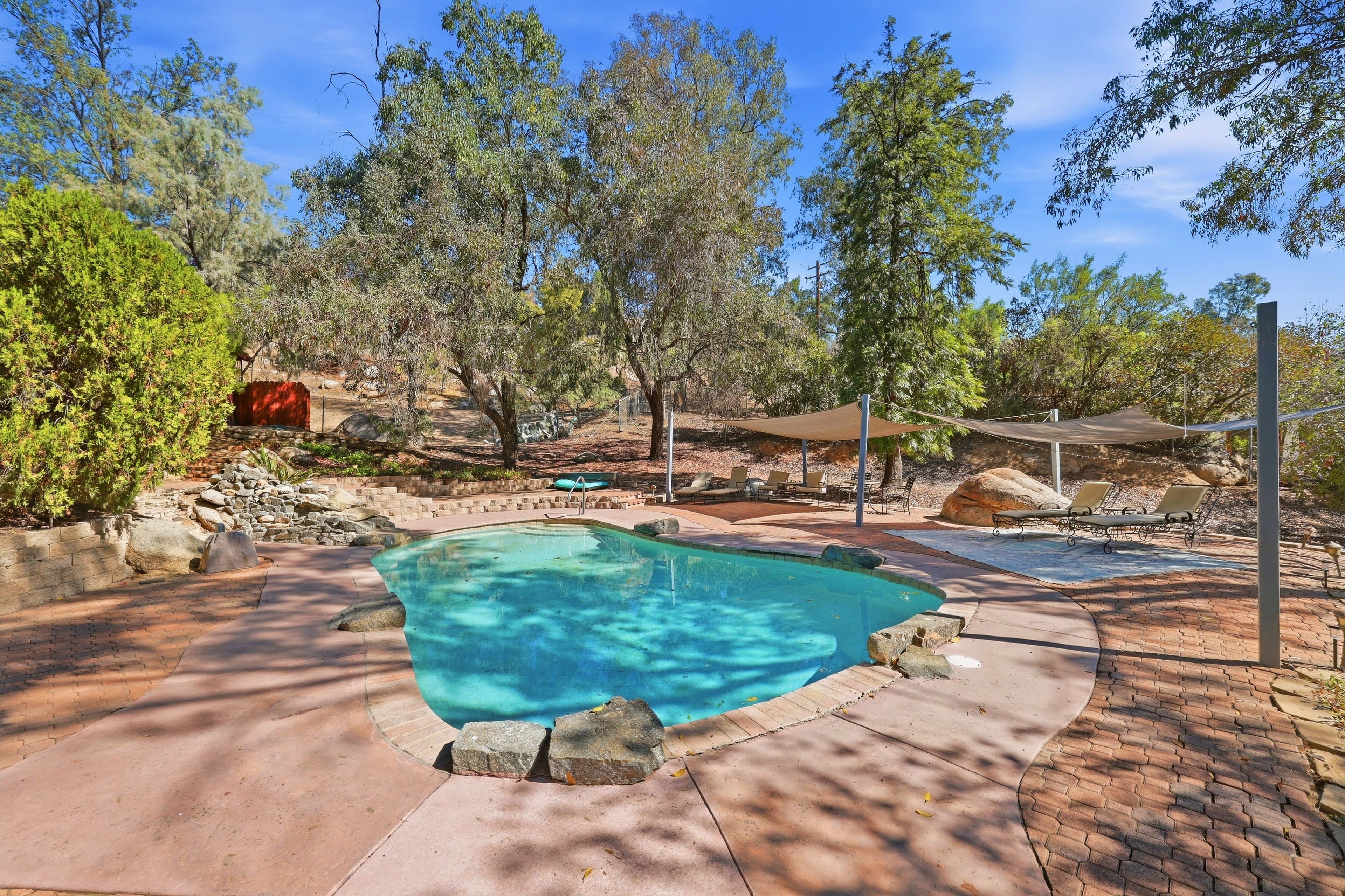 Una piscina con borde de piedra, rodeada de árboles y un patio de ladrillo.