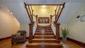 Una escalera de madera con barandilla de cristal, una planta en maceta y un cuadro en la pared.