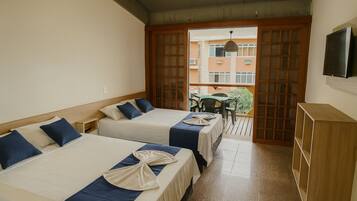 A hotel room with two beds, a TV, and a balcony with a table and chairs.