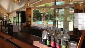 Zona de bar con vista a una piscina y follaje exterior.