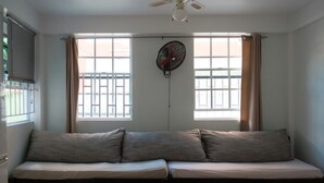 Ein Zimmer mit einer Couch, einem Deckenventilator und Fenstern mit Vorhängen.