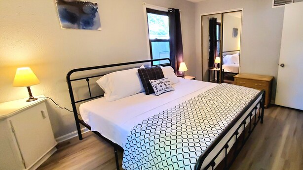 A neatly made bed with a patterned bedspread, a bedside lamp, a small table with a lamp, and a mirror on the wall. - 2 KING 3 QUEEN BEDS. Spacious. Quiet Neighborhood (Euclid)