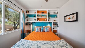 Quarto com uma cama grande, uma janela com cortinas e uma estante com diversos objetos.