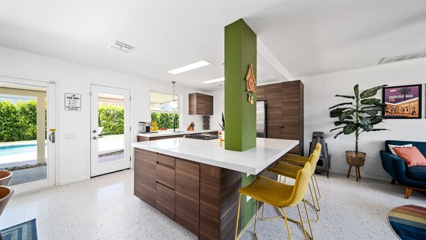 Cozinha moderna com ilha central, banquetas, área de jantar com sofá azul e vista para a piscina.