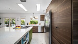 Cozinha moderna com ilha central, eletrodomésticos de aço inoxidável e vista para uma piscina através das portas de vidro.