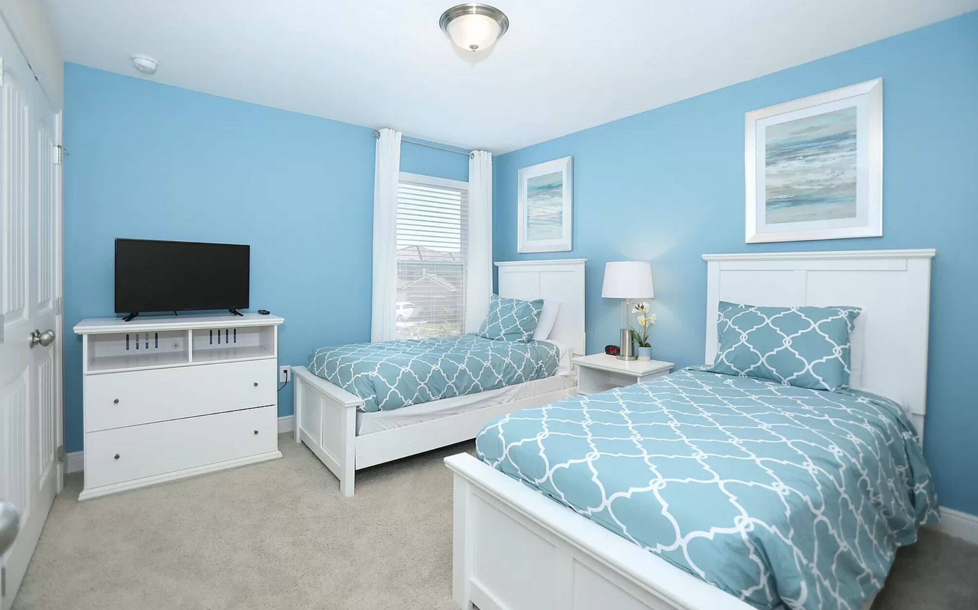 A bedroom with two beds, a TV, a dresser, and a window with blinds.