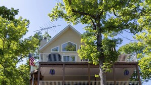 A two-story house with a balcony, a flag, and a tree in front.