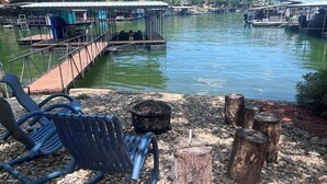 A docked boat with a covered seating area, a wooden deck, and a fire pit.