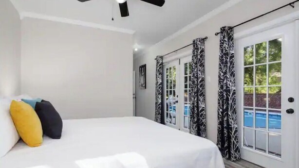 A bedroom with a bed, a ceiling fan, and a view of a swimming pool through a glass door.