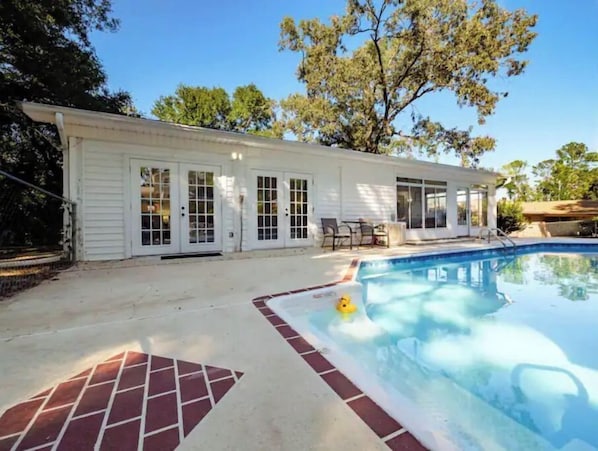 A house with a swimming pool, a covered patio, and a brick pathway leading to the pool.