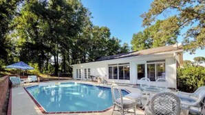 A backyard with a swimming pool, patio furniture, and a covered outdoor area.