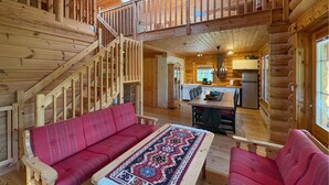 Ein Holzblockhaus-Interieur mit einer Holztreppe, einem Essbereich mit einem gemusterten Teppich und einer Küche mit einem Kühlschrank.