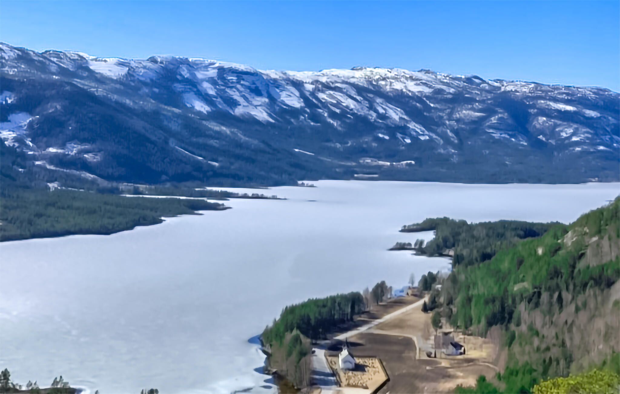 A lakeside view with a mountain backdrop, a dock, and a small building.