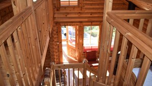 Eine Holztreppe führt zu einem Schlafzimmer im Zwischengeschoss mit Blick auf ein rotes Fahrzeug draußen.