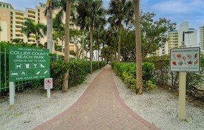 A pathway leading to Collier County Beach Park with a sign indicating it opens from 8 AM to dusk. - Steps from Beach, Fully Renovated, Pool & Tennis, Beautiful Sunset Views (Marco Island)