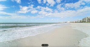 A beach with a clear sky, gentle waves, and a row of buildings along the shore. - Steps from Beach, Fully Renovated, Pool & Tennis, Beautiful Sunset Views (Marco Island)