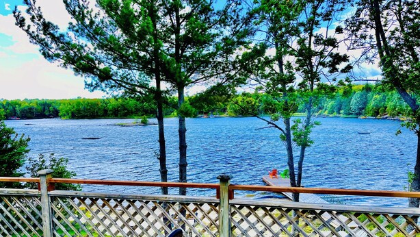 A wooden deck with a view of a lake, surrounded by trees.