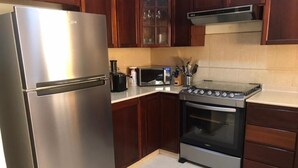 A kitchen with a stainless steel refrigerator, a microwave, a stove, and wooden cabinets. - villa Colina Bella WITH Pool behind US EMBASSY (Santo Domingo)