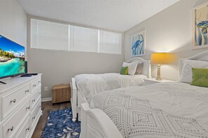 A bedroom with two beds, a TV on a dresser, and artwork on the walls.