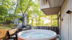 A hot tub on a wooden deck with outdoor furniture, surrounded by trees and a house.