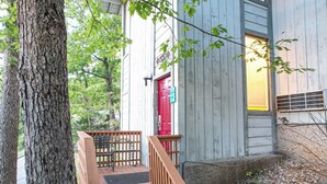 A wooden staircase leading to a red door, surrounded by trees and a wooden deck.