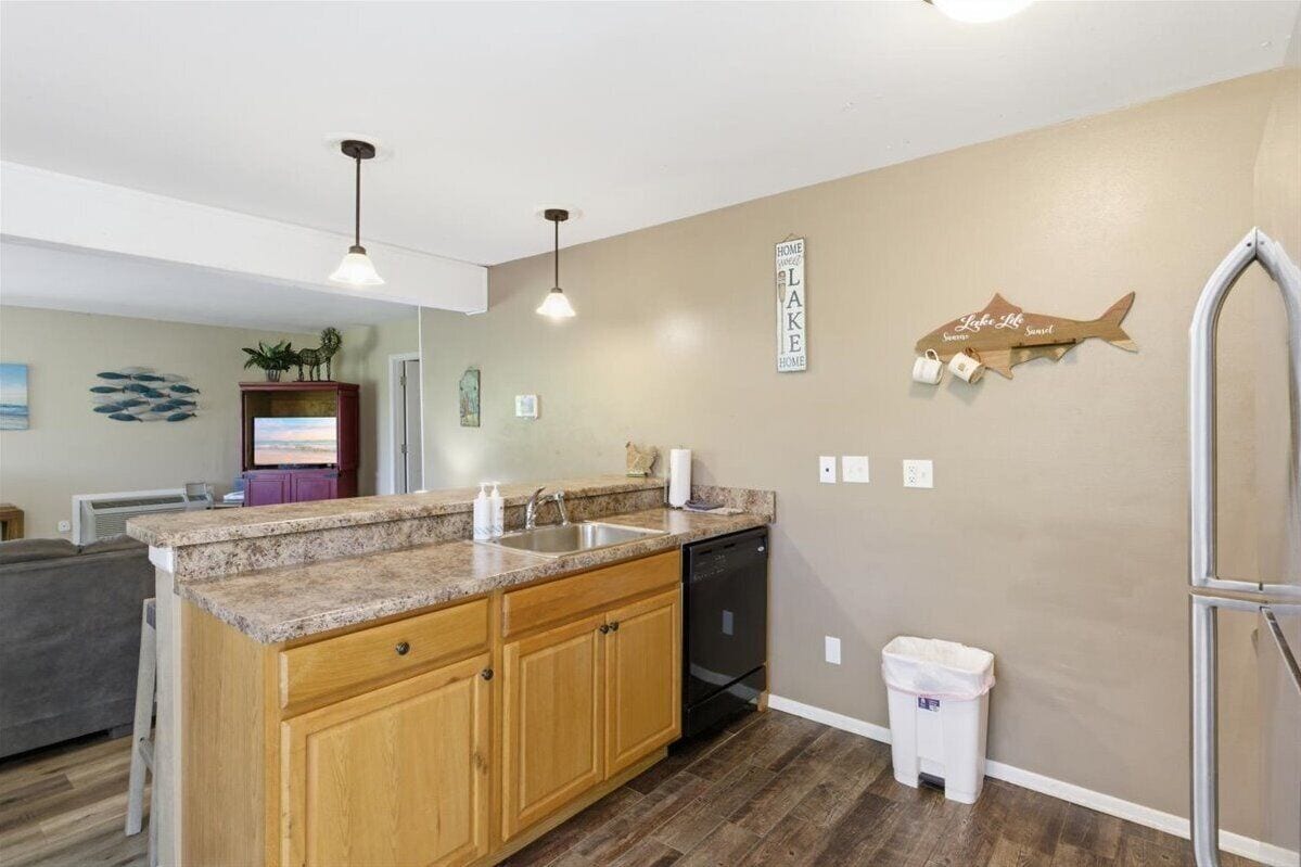 A kitchen with granite countertops, wooden cabinets, a dishwasher, and a trash can.