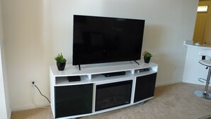 Televisor pantalla plana sobre un moble blanc per a entreteniment amb dues petites plantes en testos.