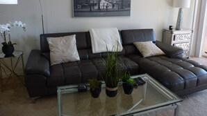 Un saló amb un sofà de cuir fosc, una taula de centre de vidre i un quadre d'una vista urbana a la paret.