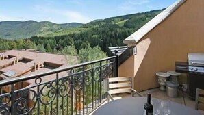 A balcony with a view of green hills, a table with chairs, and a grill.