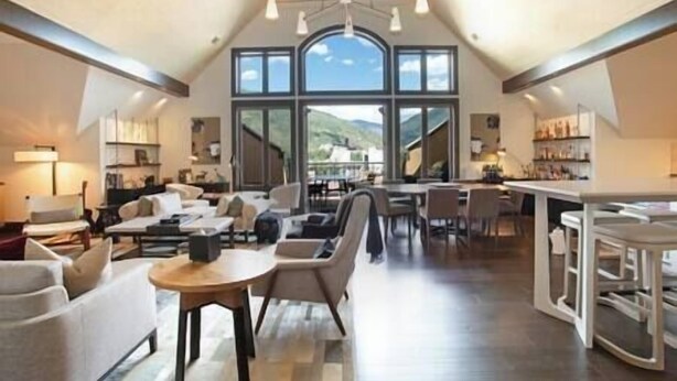 A spacious living area with a high ceiling, large windows, and a view of the outdoors.
