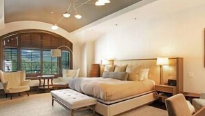 A spacious bedroom with a large bed, a sitting area with a chair and table, and a view through the window.