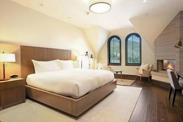 A modern bedroom with a large bed, a bedside table, a chair, and a fireplace.
