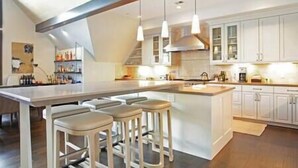 A modern kitchen with a large island, bar stools, pendant lighting, and white cabinetry.