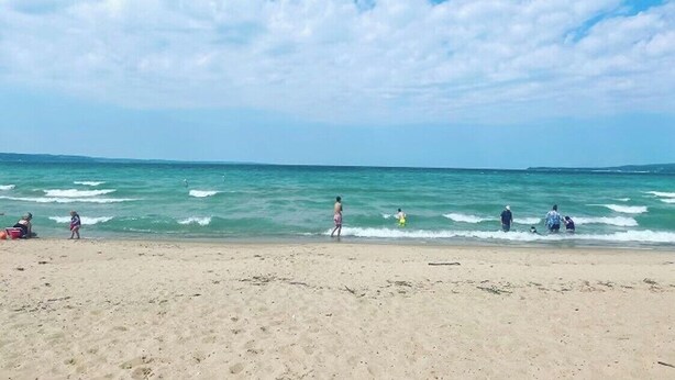 Ein Strand mit Menschen, die am Ufer entlanggehen, und einem klaren Himmel.