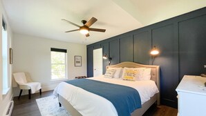 Ein Schlafzimmer mit Bett, Stuhl, Deckenventilator, Fenster und Wandleuchte.