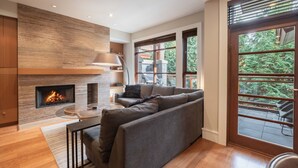 Una sala de estar moderna con chimenea, un sofá y ventanas amplias que ofrecen vistas al exterior.
