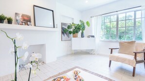 Un salón luminoso con chimenea blanca, un ventanal grande y un sillón cómodo.