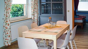 A dining area with a wooden table and white chairs, a cabinet with glass doors, and a window with floral curtains. - Awesome home in Neubrandenburg with WiFi (Neubrandenburg)